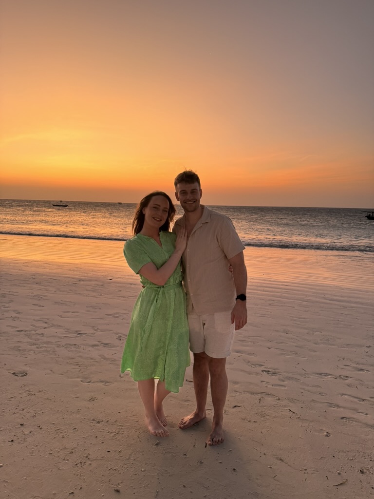Mats går ned på kne for Jenny på stranda i Zanzibar i solnedgang